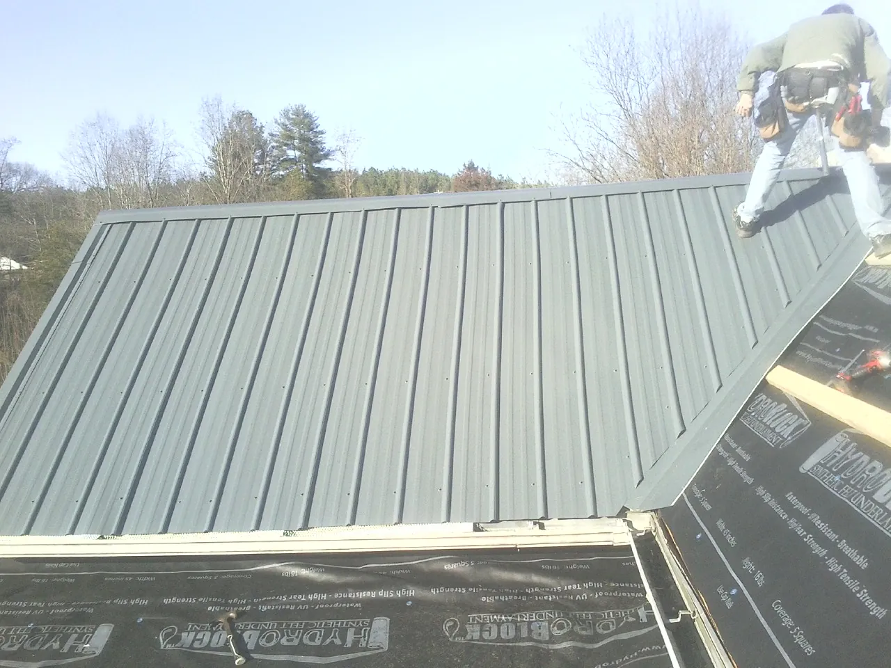 Crew installing dark green standing seam panels over synthetic underlayment in Palmer