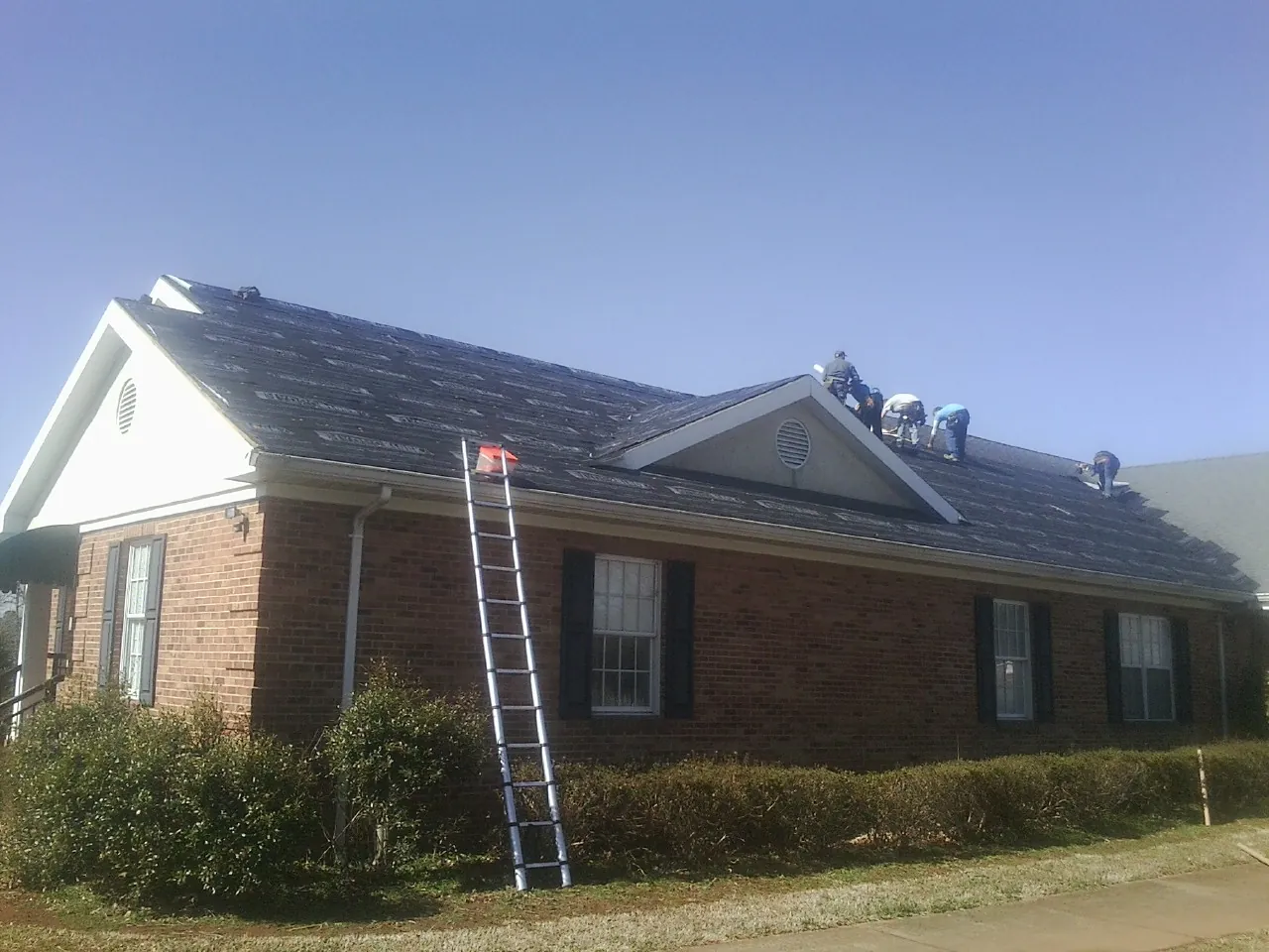 Crew tearing shingles off a brick ranch roof with a ladder set — Metal Roof Repair work by our crew in Palmer